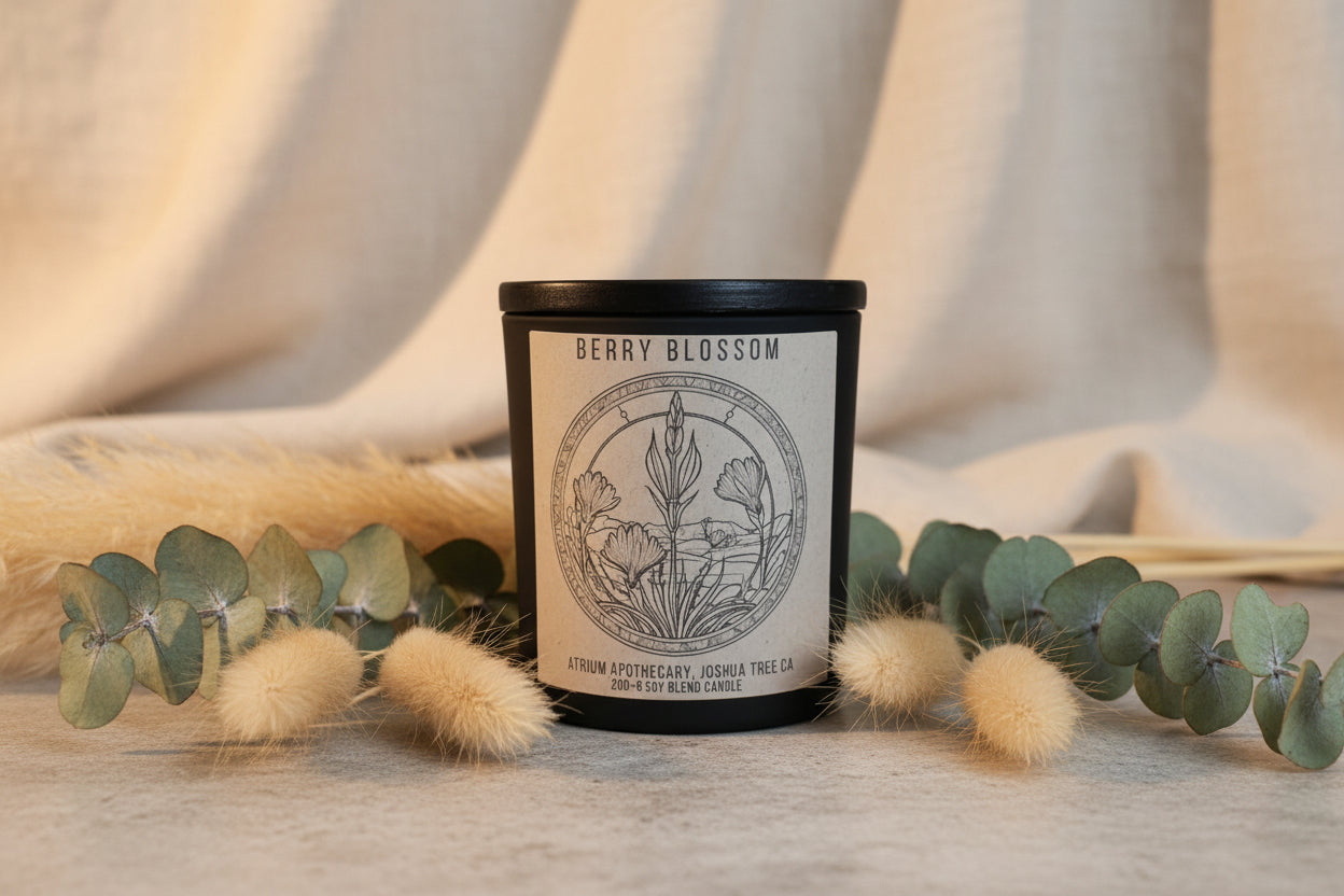 A matte black jar with a wooden lid labeled 'Berry Blossom' containing a soy blend candle, designed to evoke the scents of raspberry, orange peel, and cedar.