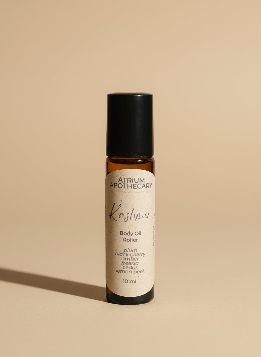 A rollerball bottle of body oil labeled 'Kashmir' by Atrium Apothecary, containing 10ml of product, placed on a white surface with a plant in the background.