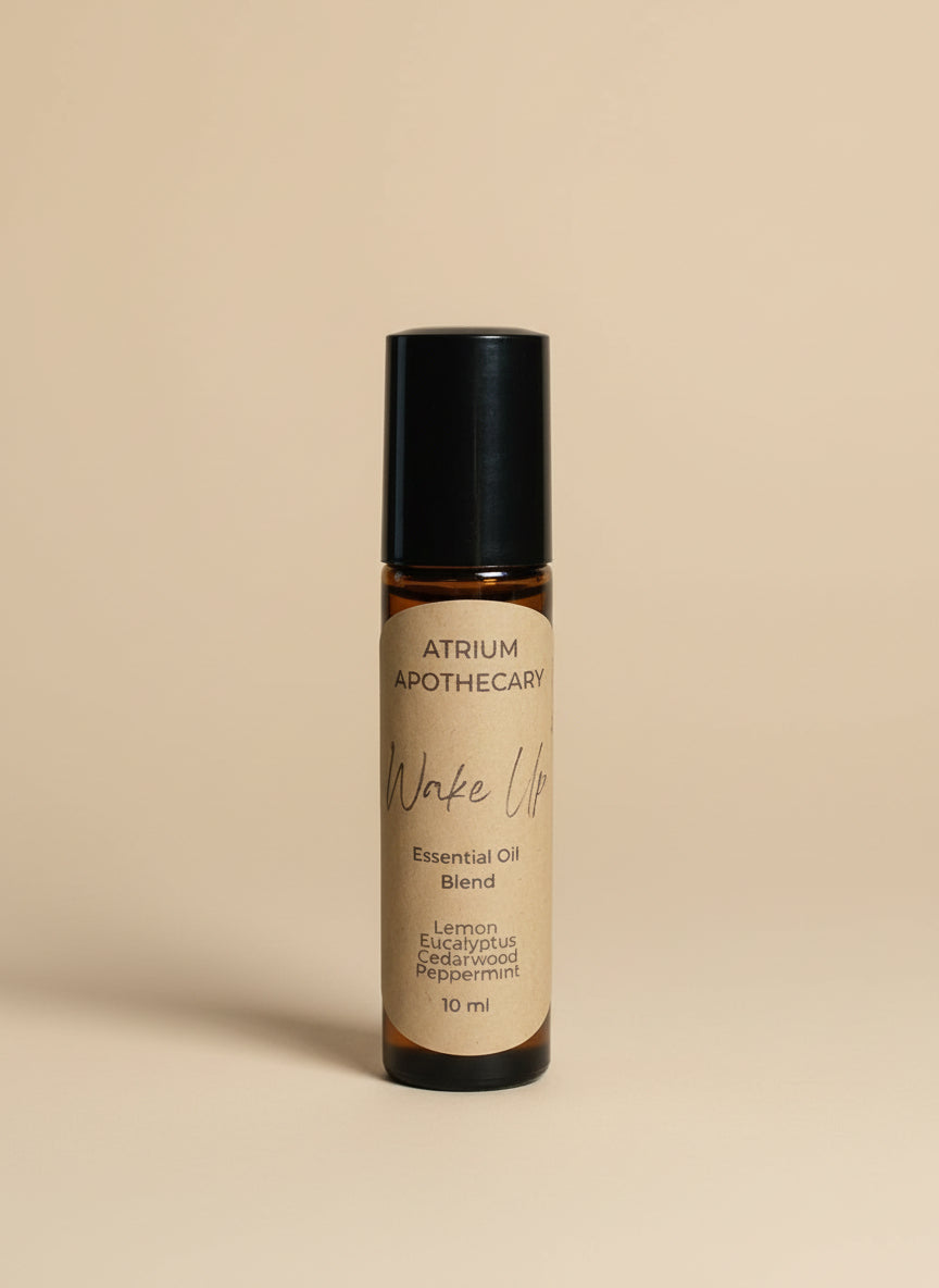 Atrium Apothecary essential oil blend bottle on a white surface with a plant and notebook in the background.