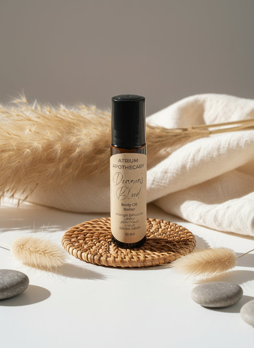 A black rollerball bottle of 'Dragon's Blood' body oil by Atrium Apothecary, sitting on a white surface, with a label that includes the product name and the scent, in a room setting.