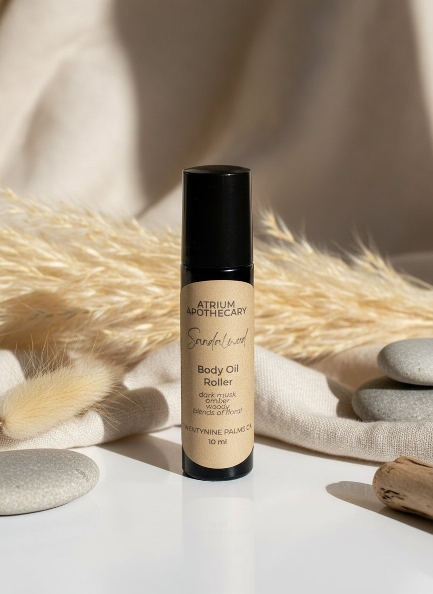 A black roller bottle of body oil labeled 'Atrium Apothecary Sandalwood Body Oil Roller' with a beige label on a white countertop.