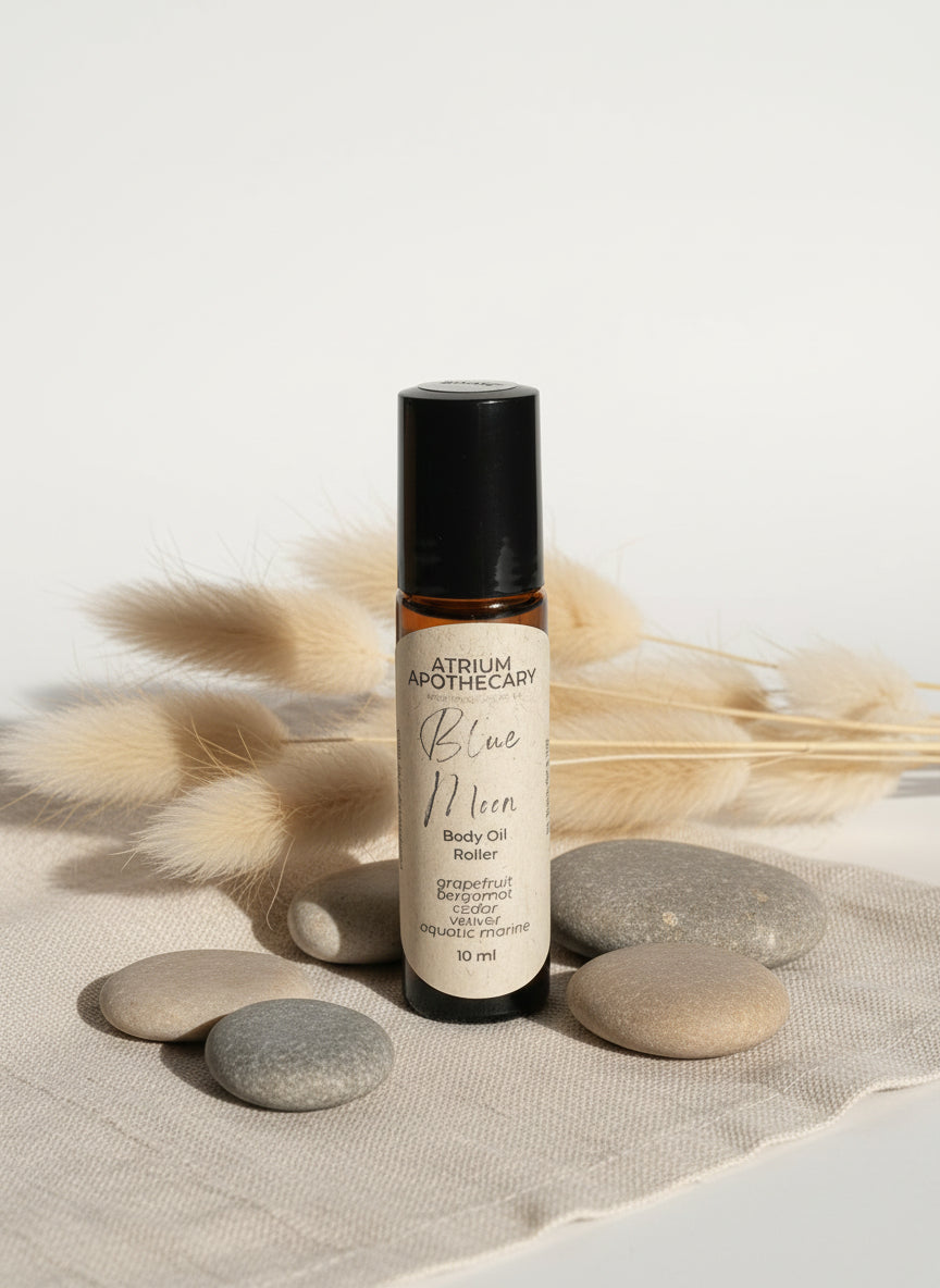 A black rollerball bottle of 'Blue Moon Body Oil' by Atrium Apothecary, labeled with white and green text, containing 10 ml of oil.