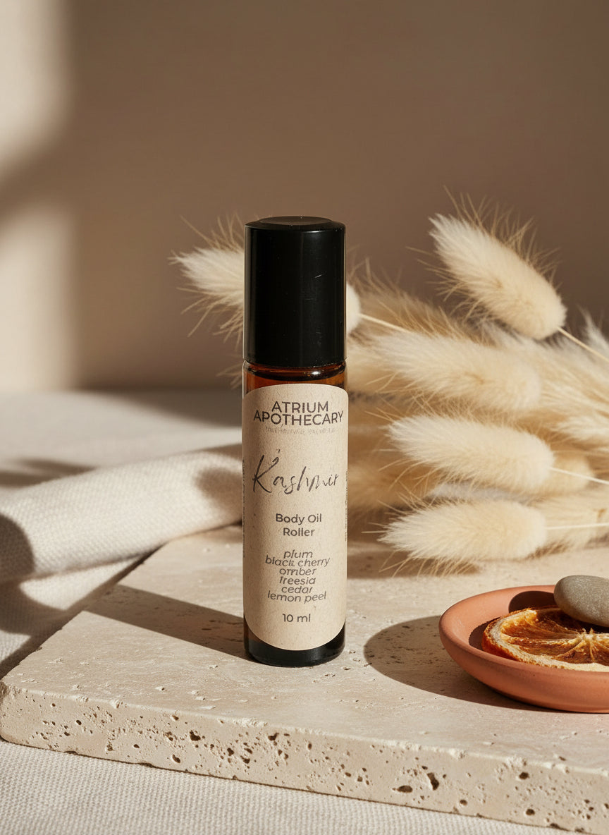 Atrium Apothecary Kashmir body oil roller on a white surface with a plant in the background